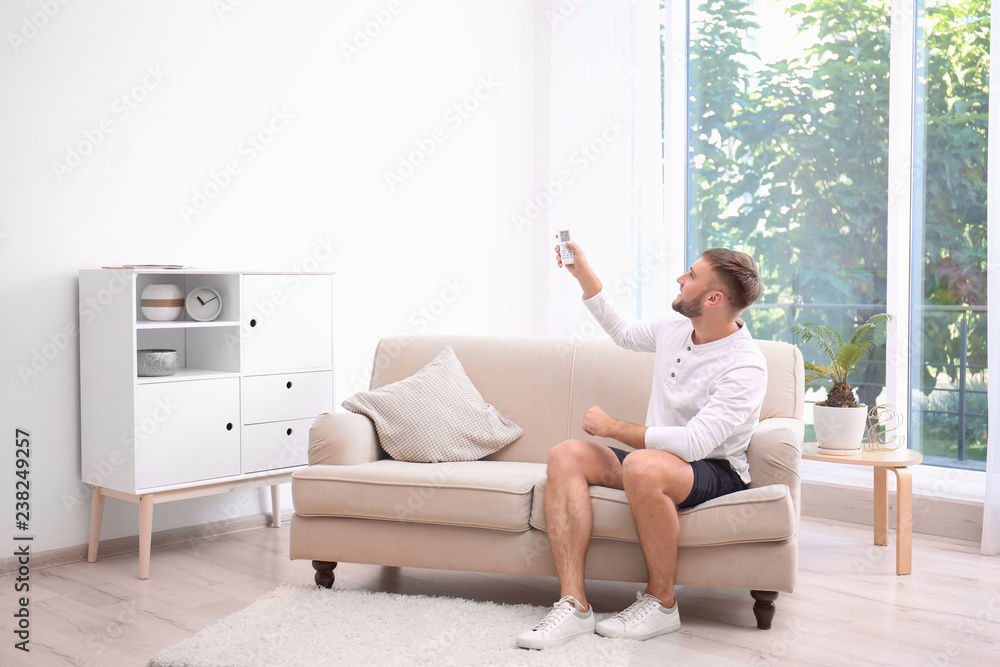 Young man with air conditioner remote at home Young man with air conditioner remote at home