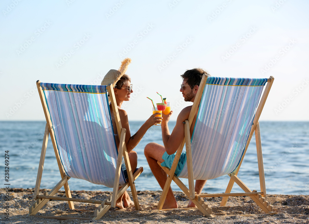 Obraz premium Young couple with cocktails in beach chairs at seacoast