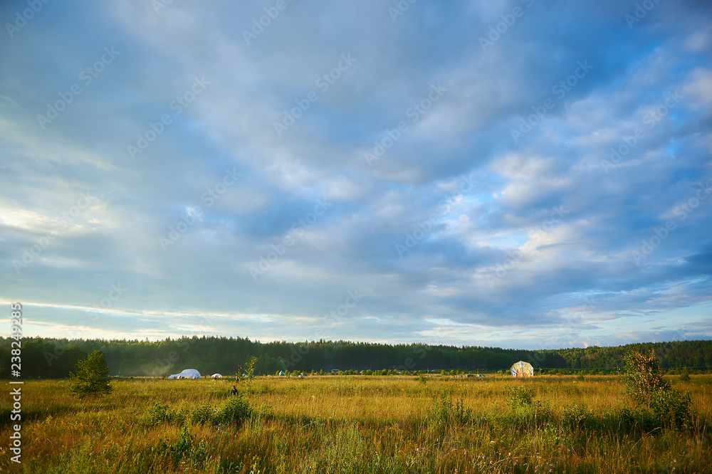 Summer landscape with field, blue cloudy sky and a camping, wide-angle