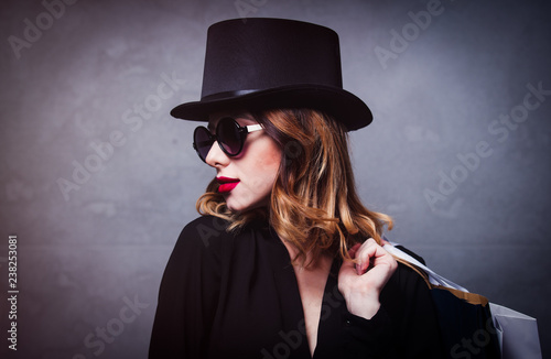 Style redhead girl in top hat with shopping bags on grey background