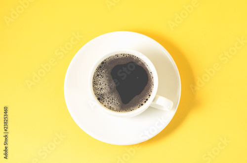 white cup with a saucer on a yellow background/white cup of espresso with a foam on a yellow background, top view