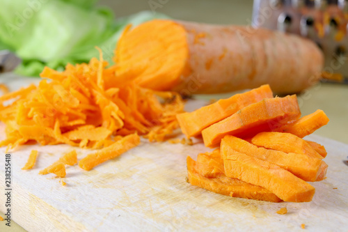 Fresh carrot grated on a metal kitchen grate. Vegetables prepared for salad with a meal on the kitchen table.