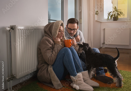 Couple with dog sitting beside radiator and freezing