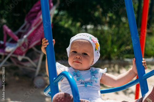 a little girl sits in the arms of a girl, she is hugged behind her back and holding hands.little girl in a white dress and hat riding on a swing, summer sun and heat. playground. childhood serenity