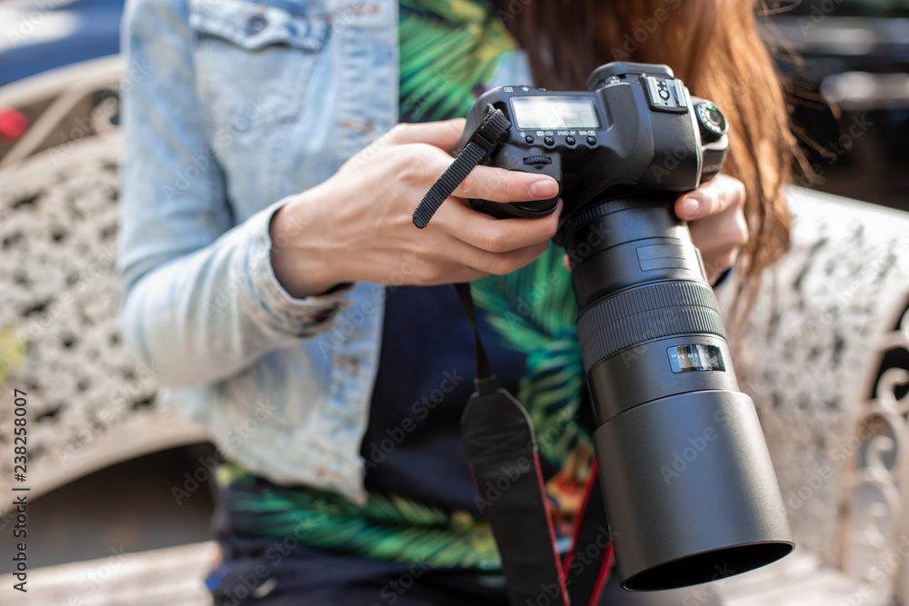 Fototapeta premium Close-up of female hands holding a professional camera. Female photographer with a professional camera.