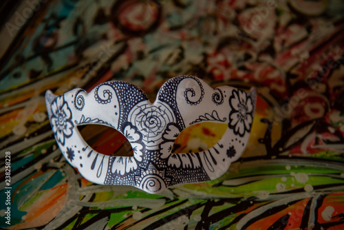 White carnival mask with artistic drawings in black color on old colored wooden table.