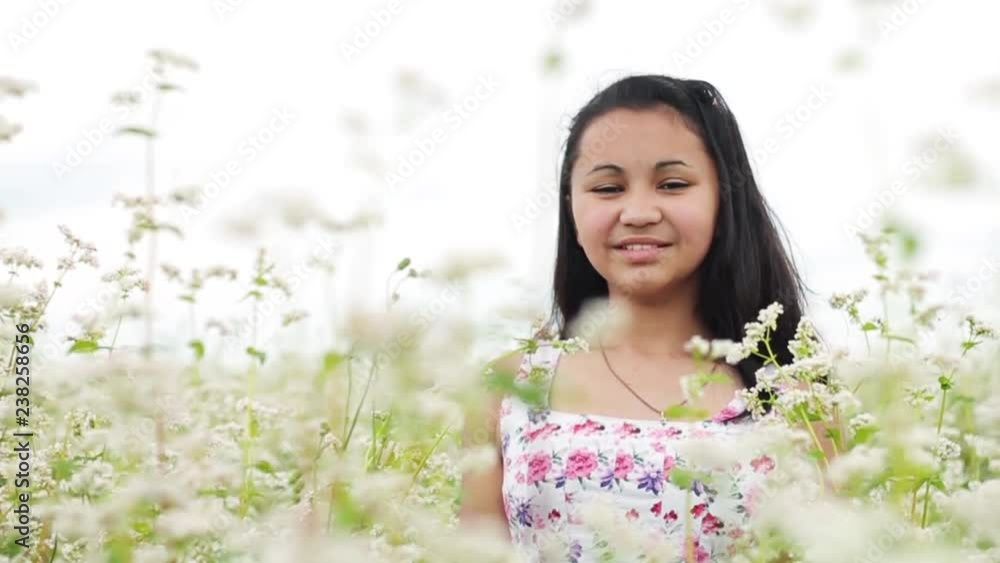 Lovely young woman smiling straight to camera through the blooming white summer wild flowers. Enjoying life, happiness, positive emotions. Beautiful landscape. Female portrait Lovely young woman smiling straight to camera through the blooming white summer wild flowers. Enjoying life, happiness, positive emotions. Beautiful landscape. Female portrait