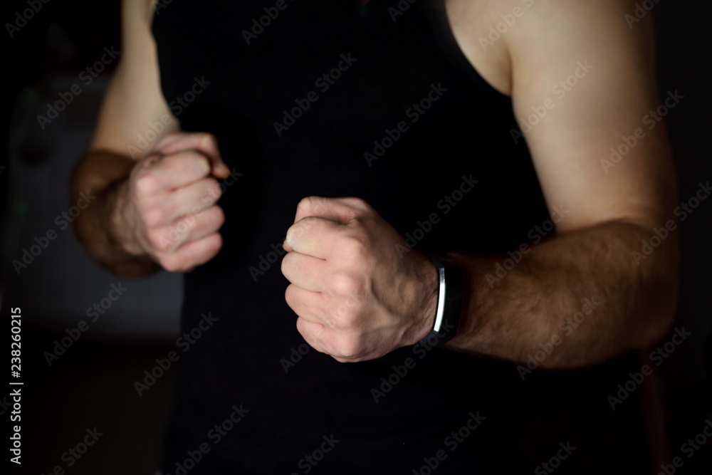 Male hands in a boxing rack with fists in a black T-shirt on a dark black background, as a symbol of the fight Male hands in a boxing rack with fists in a black T-shirt on a dark black background, as a symbol of the fight