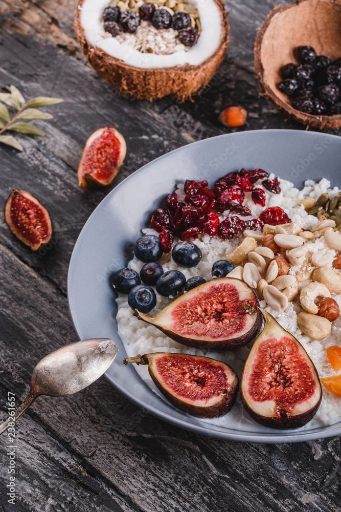 Rice coconut porridge with figs, berries, nuts, dried apricots and coconut milk in plate on rustic wooden background. Healthy breakfast ingredients. Clean eating, vegan food concept, close up