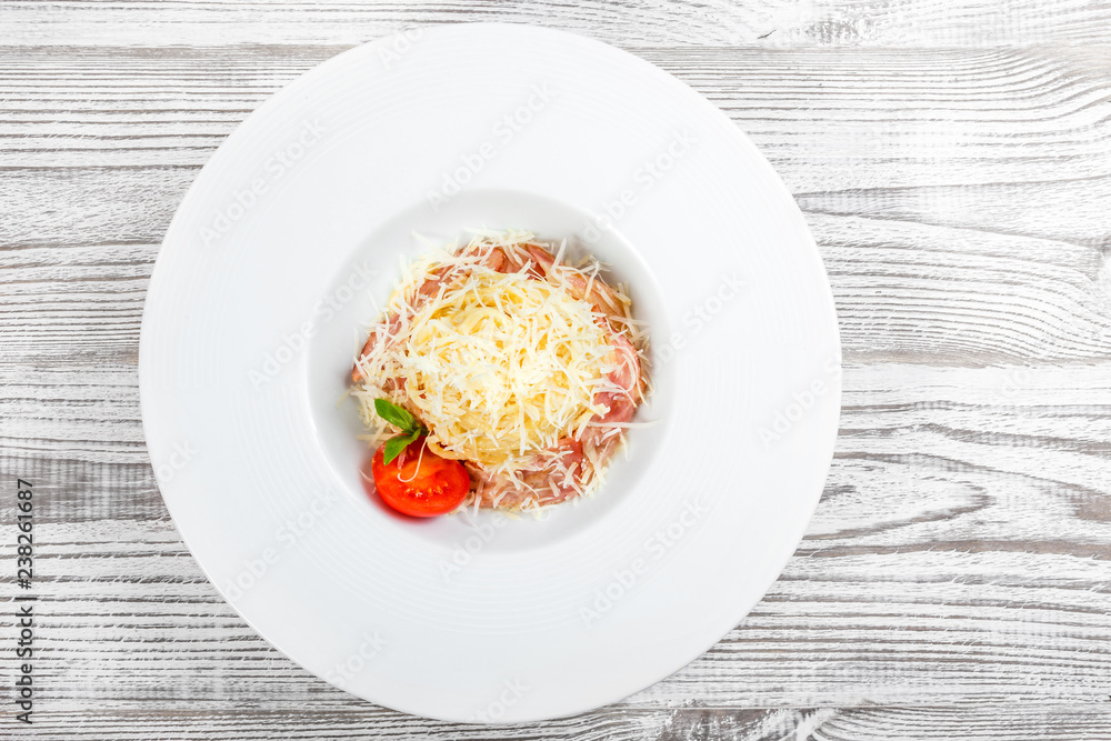 Fettuccine pasta with meat, ham, parmesan cheese, basil and tomato on plate on light wooden background, Italian cuisine. Ingredients on table