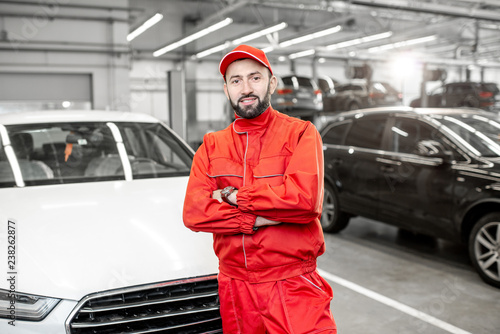 Portrait of a handsome auto mechanic in red uniform standing at the car service