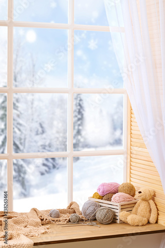 Woolen yarn and fabric on the window sill. Beautiful view outside the window - winter landscape and snow.