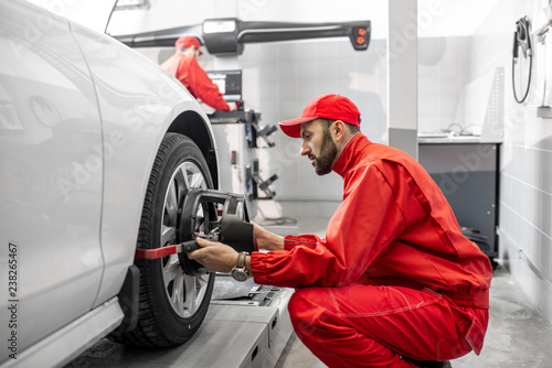 Handsome auto mechanic in red uniform fixing disk for wheel alignment at the car service photo