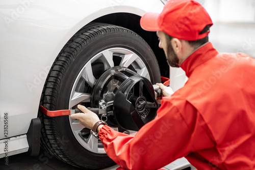 Handsome auto mechanic in red uniform fixing disk for wheel alignment at the car service © rh2010