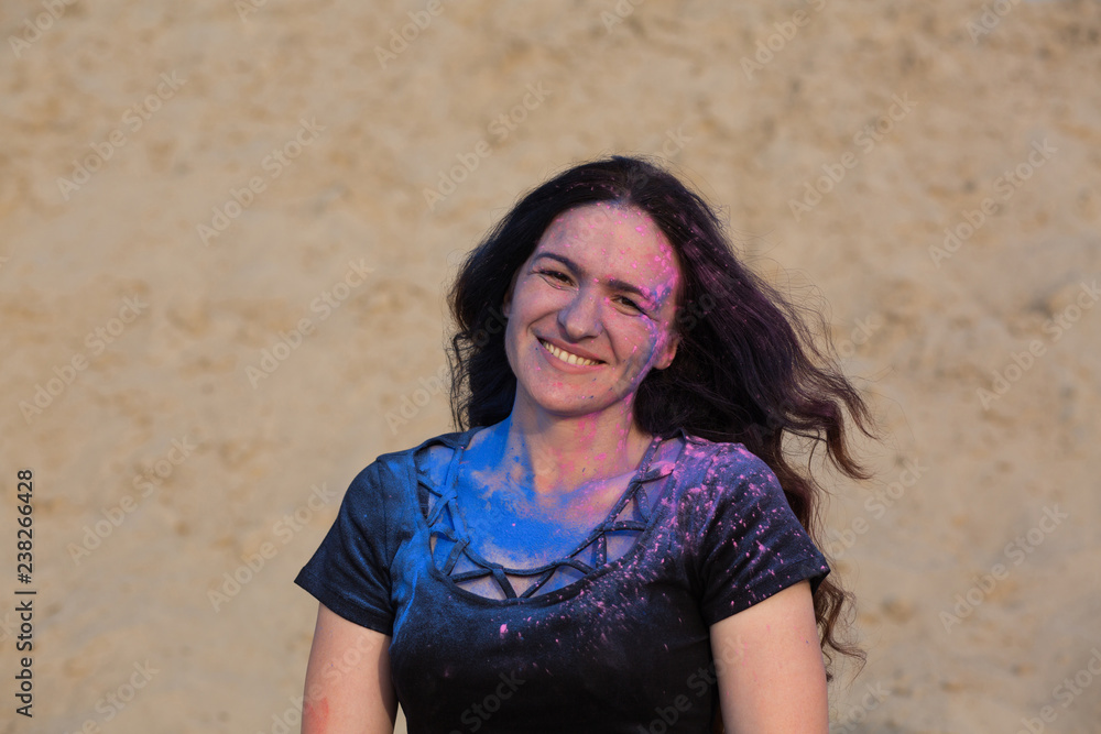 Closeup shot of cheerful brunette model with long curly hair covered with colorful dry paint Holi at the desert Closeup shot of cheerful brunette model with long curly hair covered with colorful dry paint Holi at the desert