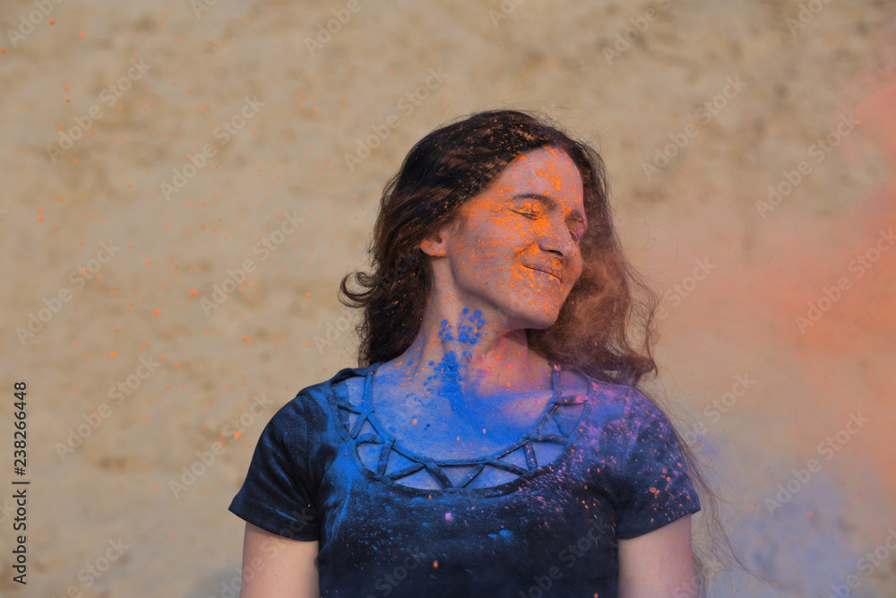 Closeup shot of pleased brunette woman with long curly hair covered with colorful dry paint Holi at the desert