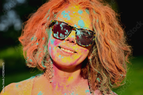Merry redhead model with curly hair covered with colorful paint at the park
