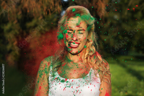 Cool blonde girl wearing white shirt and posing covered with dry paint at the Holi Festival