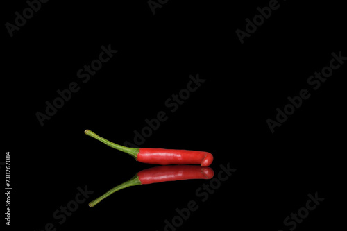 Small hot pod of red chili peppers on a black background with bright and clear reflection in the glass.