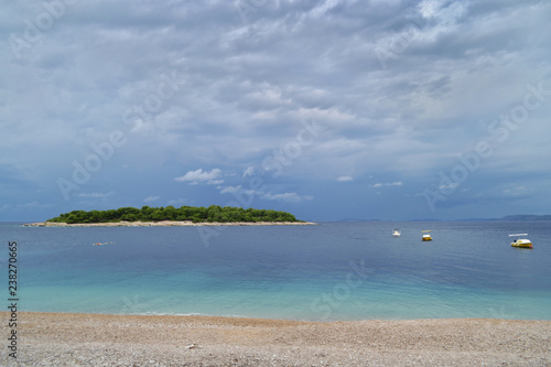 A green island in the azure sea. Beach, boats and cloudy sky. Primosten, Croatia,