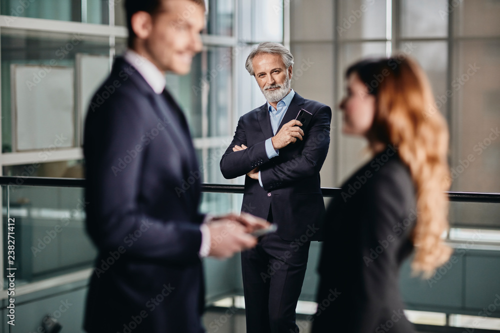 handsome senior business man observing his younger colleagues and looking at his phone handsome senior business man observing his younger colleagues and looking at his phone