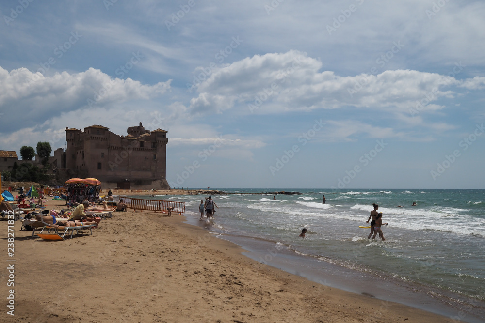 Seaside scene, people sunbathing and swimming in the sea with a castle in the distance