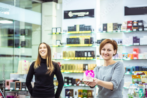 Positive smiling pleasant salesgirls suggesting perfume in modern cosmetic store. successful sellers. Free Download Positive smiling pleasant salesgirls suggesting perfume in modern cosmetic store. successful sellers. - GFXLoad