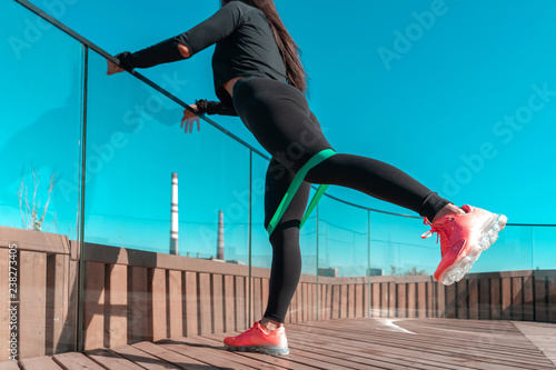 Woman stretching and exercising outdoors with rubber band in urban environment.