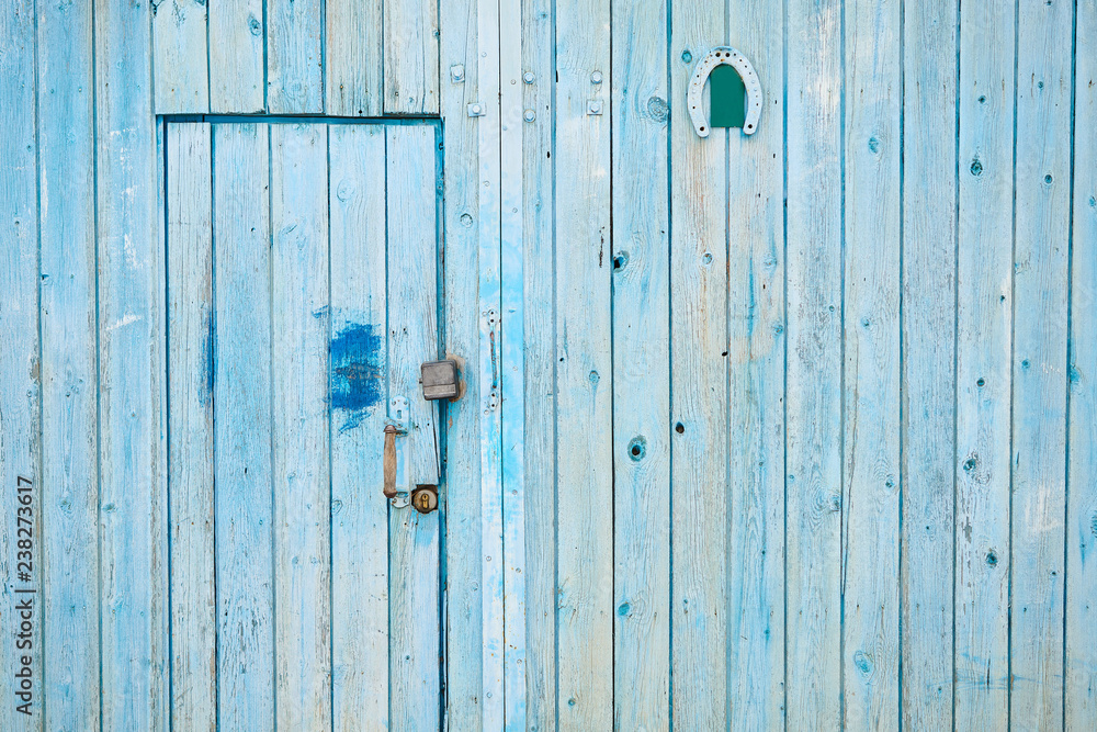 A textured blue wooden wall with locked door and horseshoe A textured blue wooden wall with locked door and horseshoe