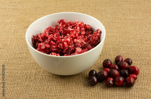Chopped fresh raw cranberries in white bowl with whole cranberries on side