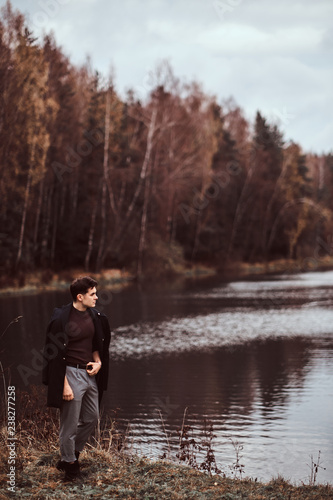 A handsome young man standing near a lake in the autumn forest.