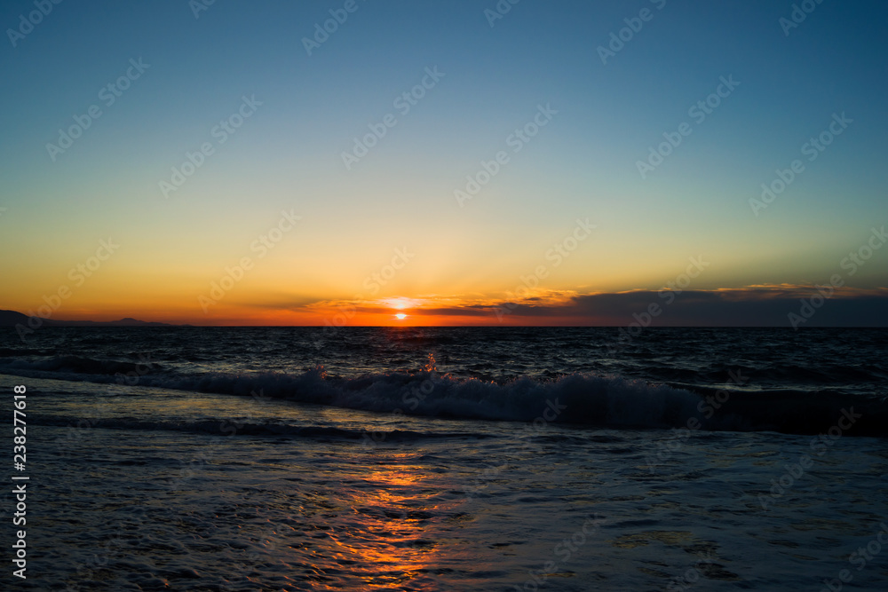 Naklejka premium The setting sun over the horizon at sea. Reflection of sunlight in the water. Small waves with foam.