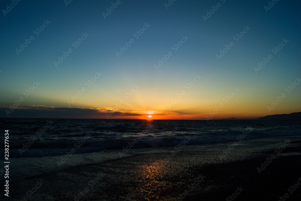 Rays of the sun during sunset on the sea. The sun above the horizon. Beach with small waves. Reflection of sunlight in the water.