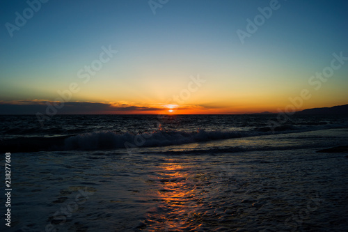 Evening sun during sunset at sea. Beach with small waves and foam. Reflection of sunlight in the water.