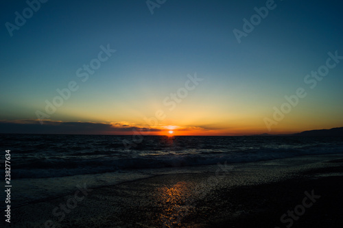 Rays of the sun during sunset on the sea. The sun above the horizon. Beach with small waves. Reflection of sunlight in the water. © isuhi