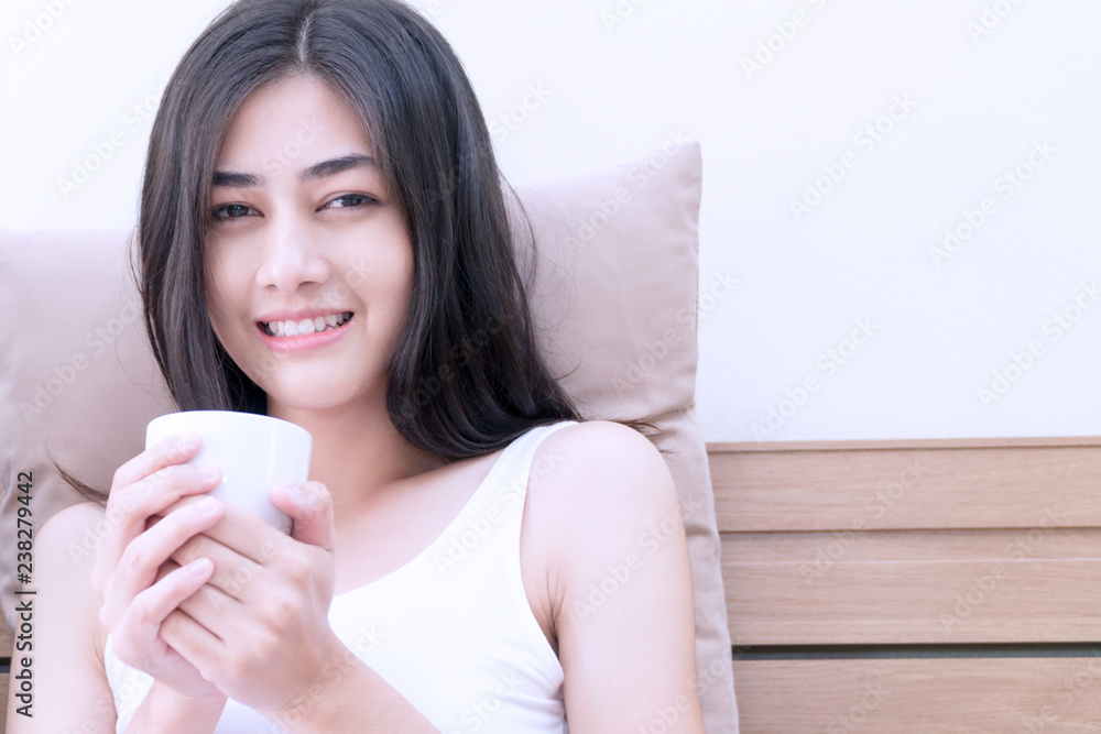 Cheerful smile young woman holding white cup of coffee in her hands on the bad in morning with copy space. Lifestyle concept Cheerful smile young woman holding white cup of coffee in her hands on the bad in morning with copy space. Lifestyle concept