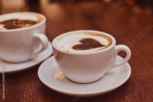 Two cups of hot coffee with art on the wooden table in a coffee shop  blur background with bokeh effect