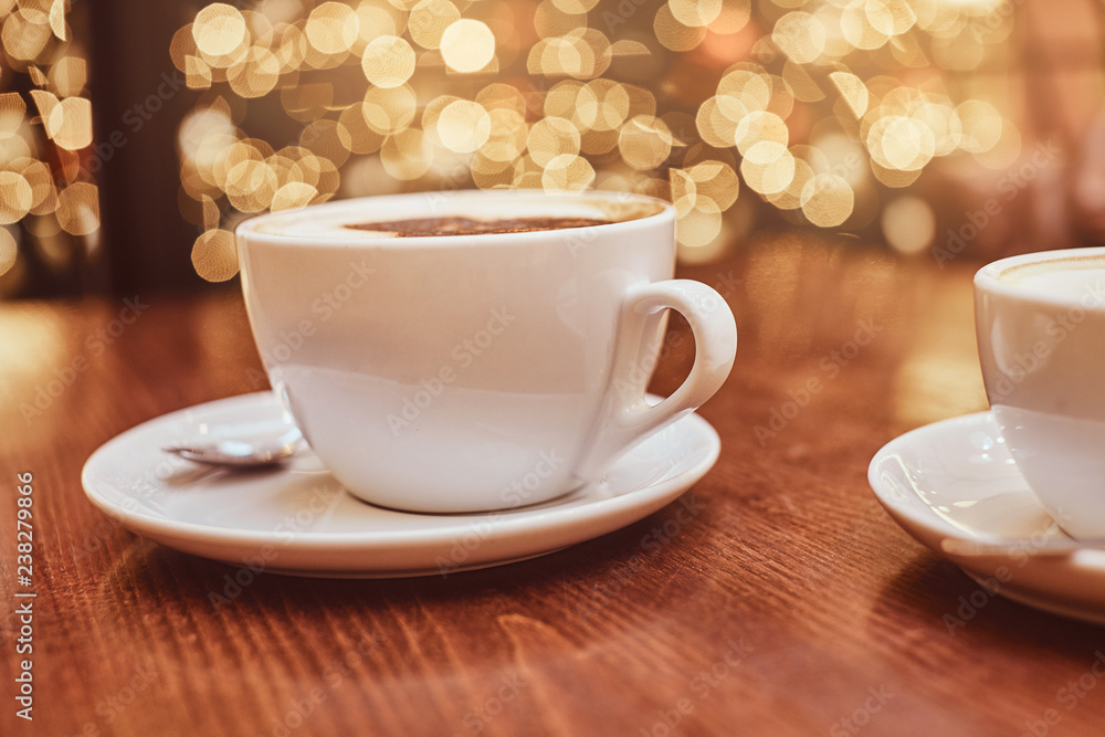 Hot coffee with art in a cup on the wooden table in a coffee shop, blur background with bokeh effect Hot coffee with art in a cup on the wooden table in a coffee shop, blur background with bokeh effect