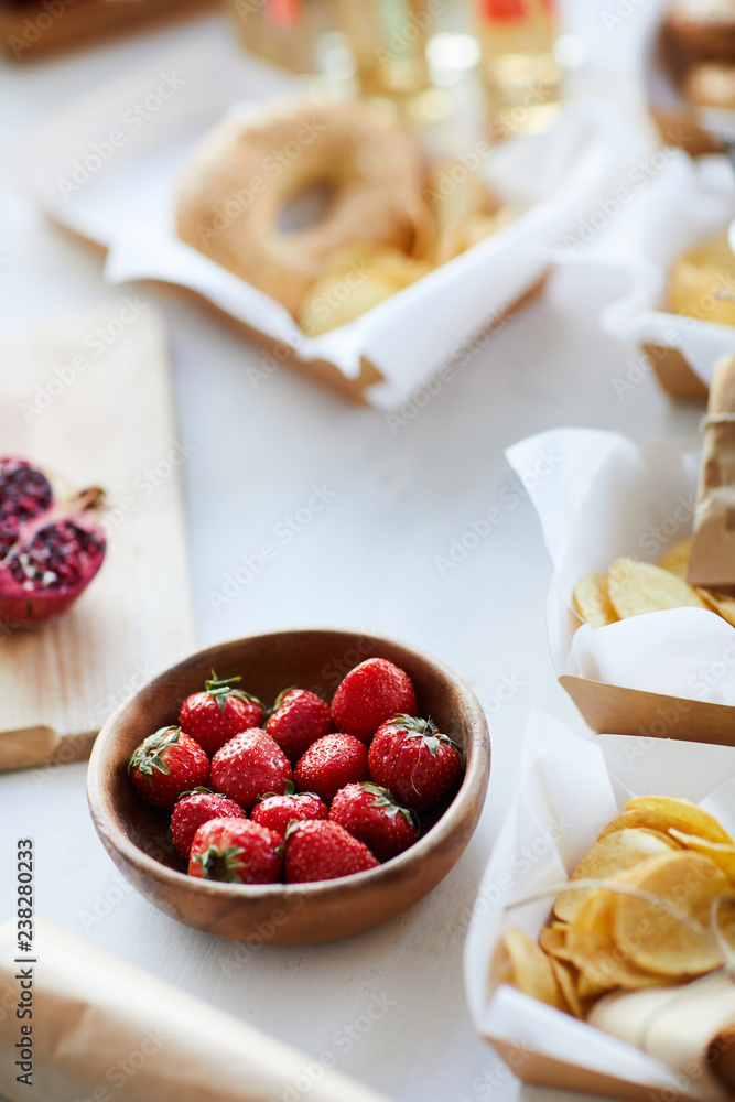 High angle background of rustic table with delicious strawberries in wooden bowl and various snacks for party, copy space High angle background of rustic table with delicious strawberries in wooden bowl and various snacks for party, copy space