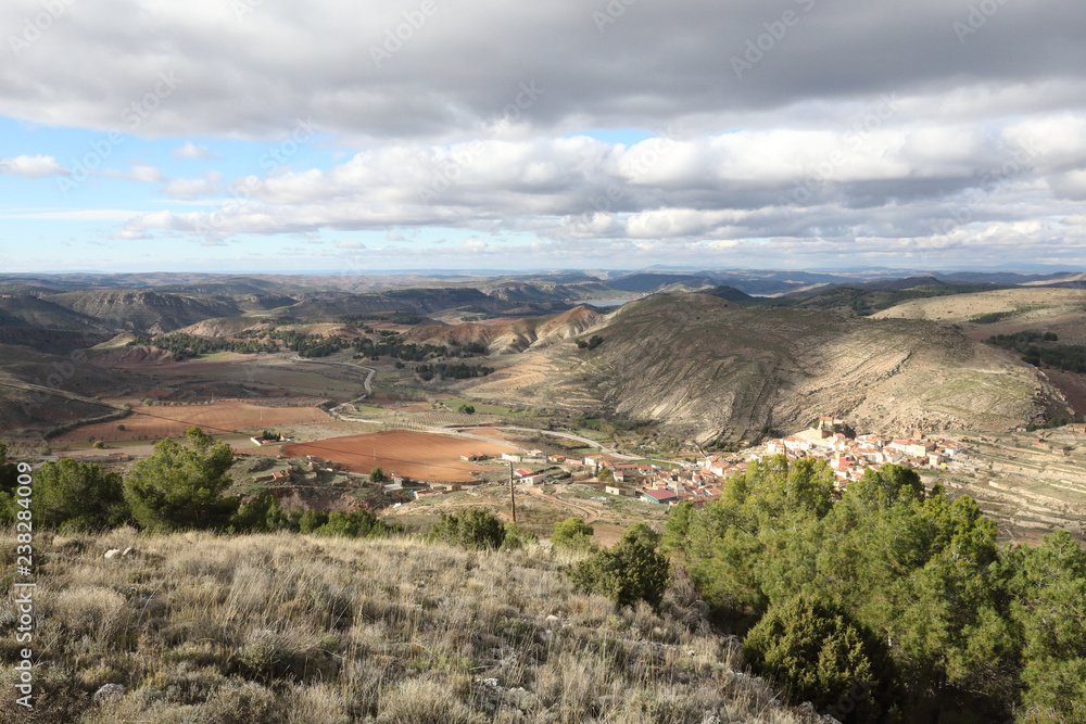 A landscape of the small rural town of Monterde, in the Aragon countryside, among hills and pastures, in a sunny autumn with clouds, in Spain