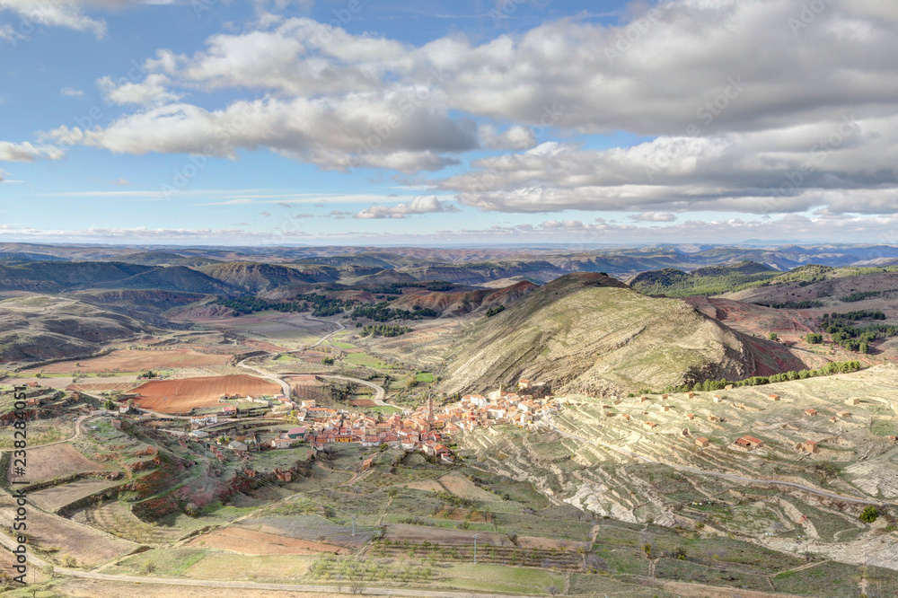 Naklejka premium A landscape of the small rural town of Monterde, in the Aragon countryside, among hills and pastures, in a sunny autumn with clouds, in Spain