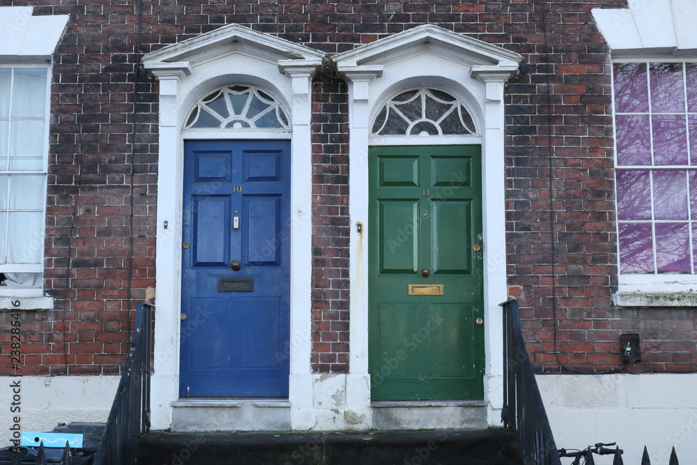 A blue and a green traditional English doors with white borders on a brick wall of a terrace house in Bristol, United Kingdom A blue and a green traditional English doors with white borders on a brick wall of a terrace house in Bristol, United Kingdom