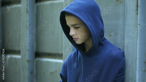 Upset pallid boy hiding behind fence, victim of bullying, underage drug addict