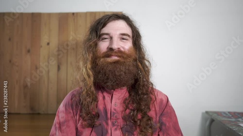 Long haired hipster hippie type man solo indoors simply smiling into camera