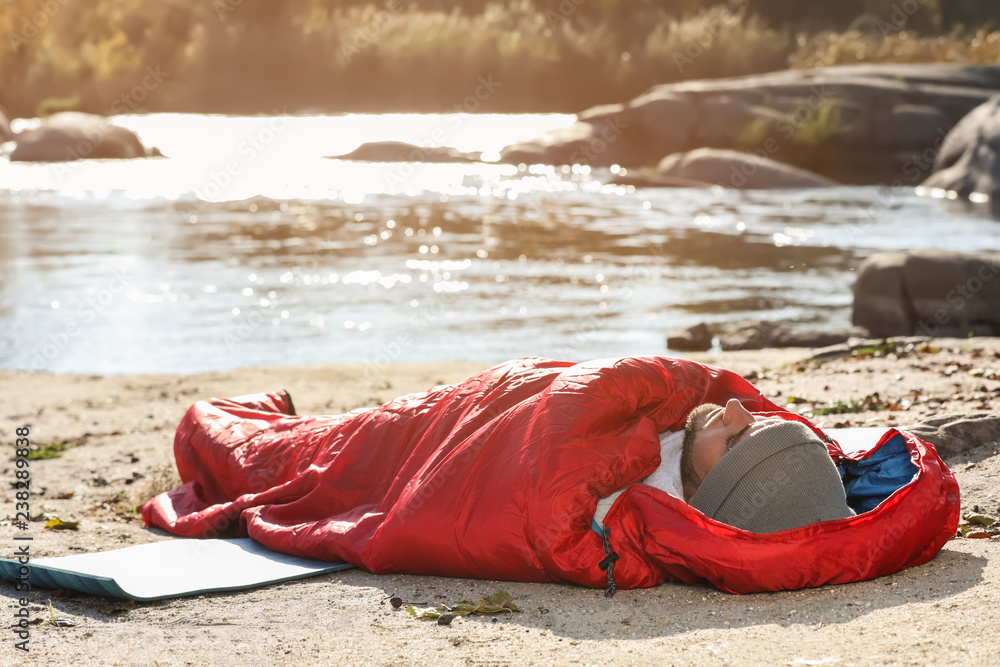 Man in sleeping bag on wild beach. Camping equipment