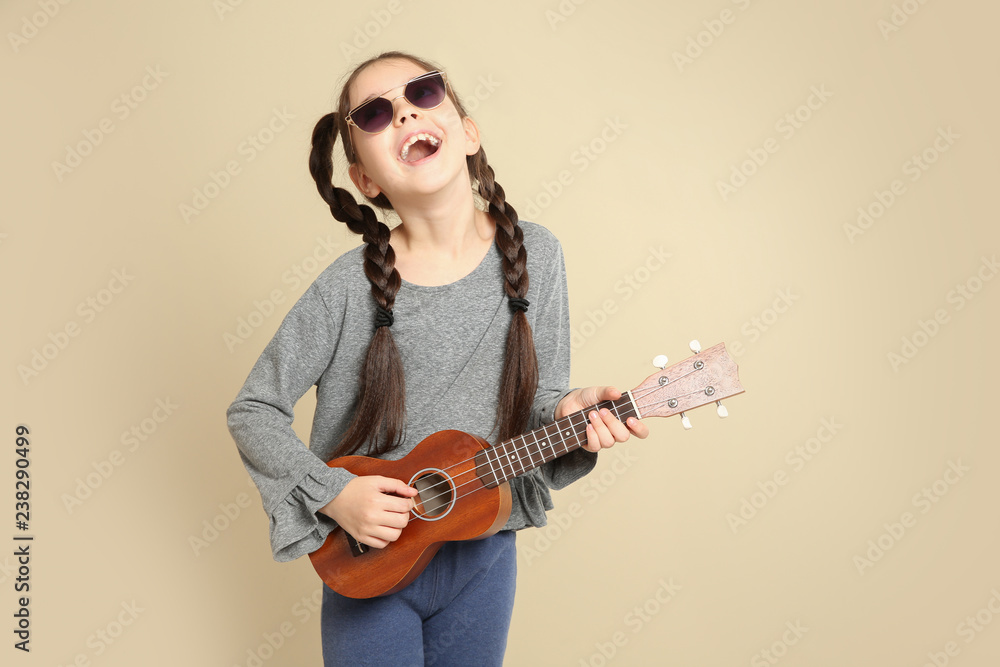 Portrait of little cheerful girl playing guitar on color background