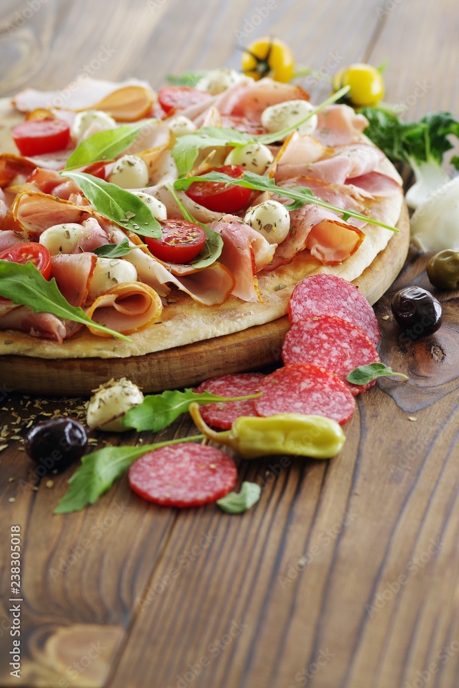 Pizza on a wooden table, with prosciutto ham, mozzarella and various ingredients.