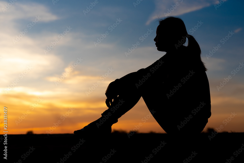 Silhouette of sad and depressed women sitting at walkway of park with sunset