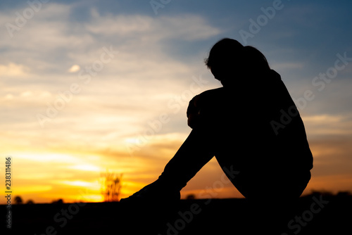 Silhouette of sad and depressed women sitting at walkway of park with sunset