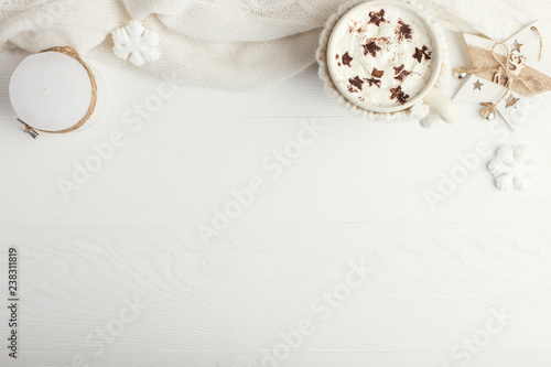 A cup of hot winter drink with whipped cream and a dusting powder with an asterisk, white snowflakes and knitted scarf on a wooden table. Christmas concept in bright colors. Copy space.